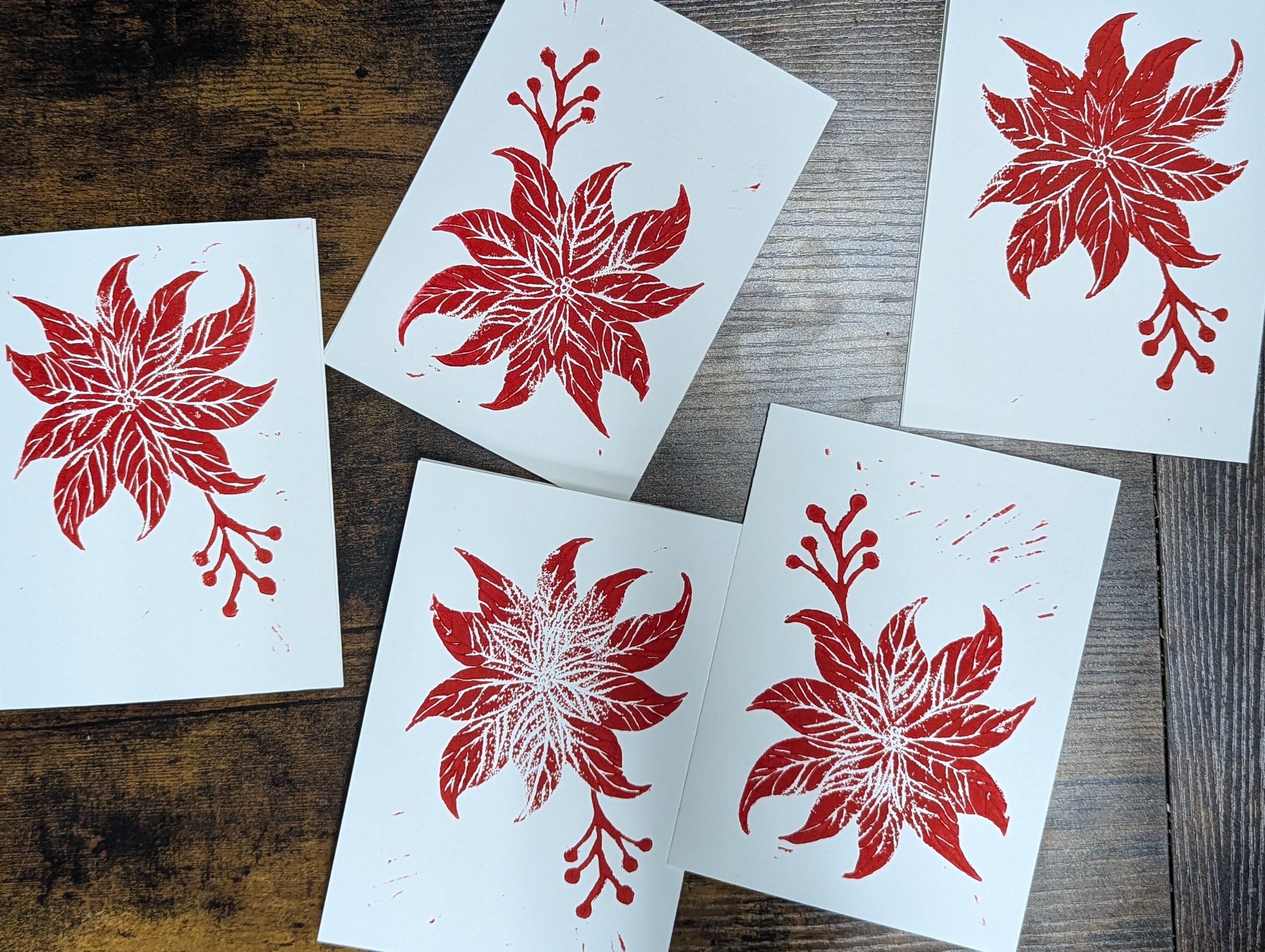 Five white cards with red floral designs on a wooden surface